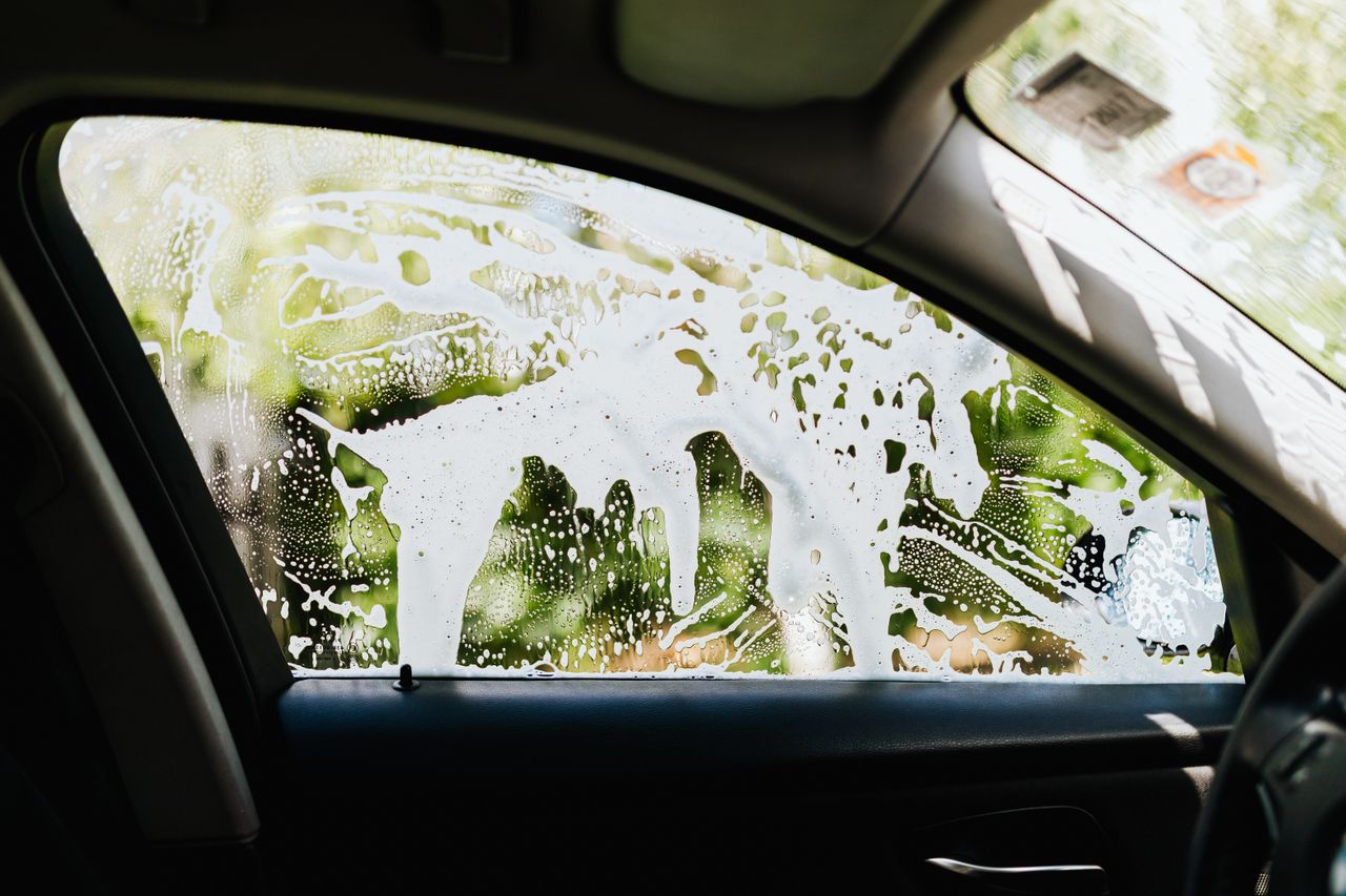 services-01 Vue depuis l'intérieur d'une voiture, avec de l'eau savonneuse sur la vitre pendant un lavage auto.